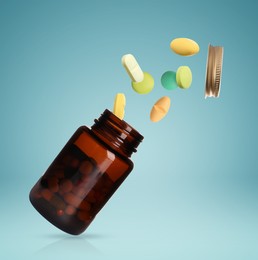 Image of Many different colorful pills bursting out of bottle on light blue background