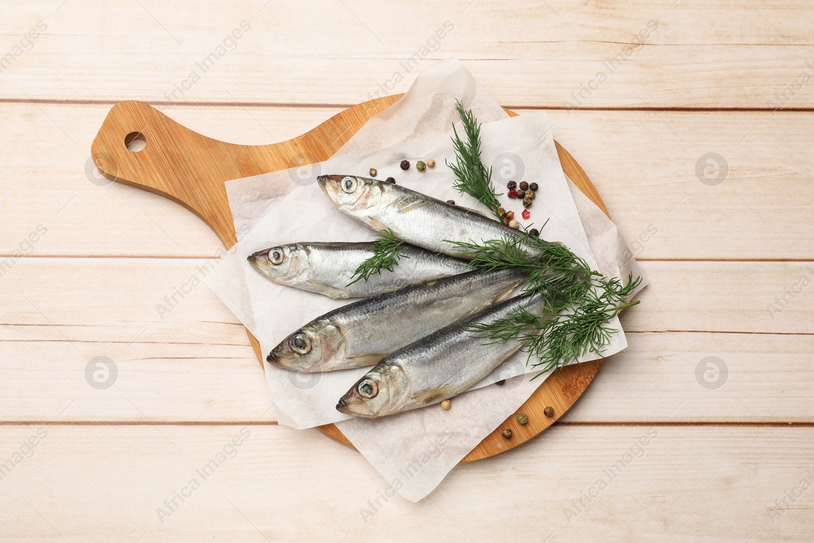 Photo of Fresh raw sprats, peppercorns and dill on light wooden table, top view