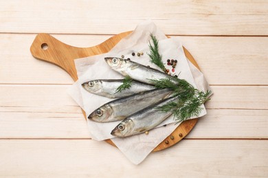 Photo of Fresh raw sprats, peppercorns and dill on light wooden table, top view