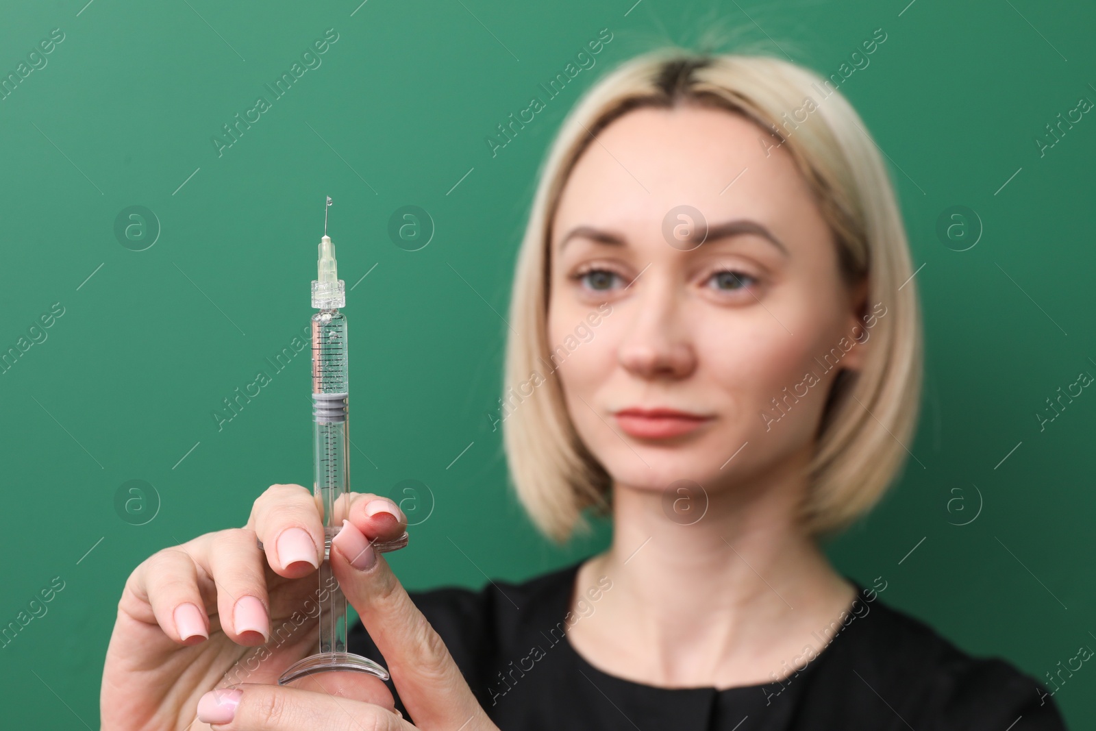 Photo of Cosmetologist with syringe on green background, selective focus