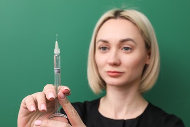 Cosmetologist with syringe on green background, selective focus