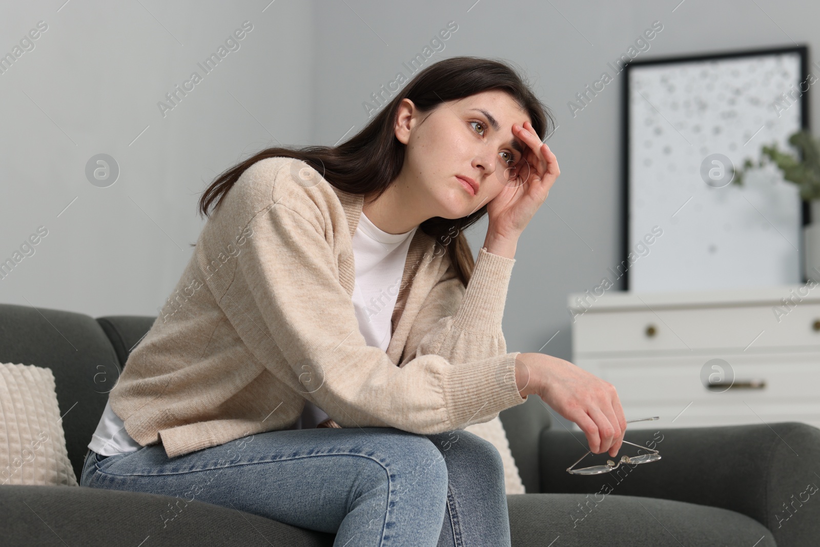 Photo of Overwhelmed woman with glasses sitting on sofa at home