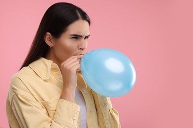 Woman inflating light blue balloon on pink background, space for text