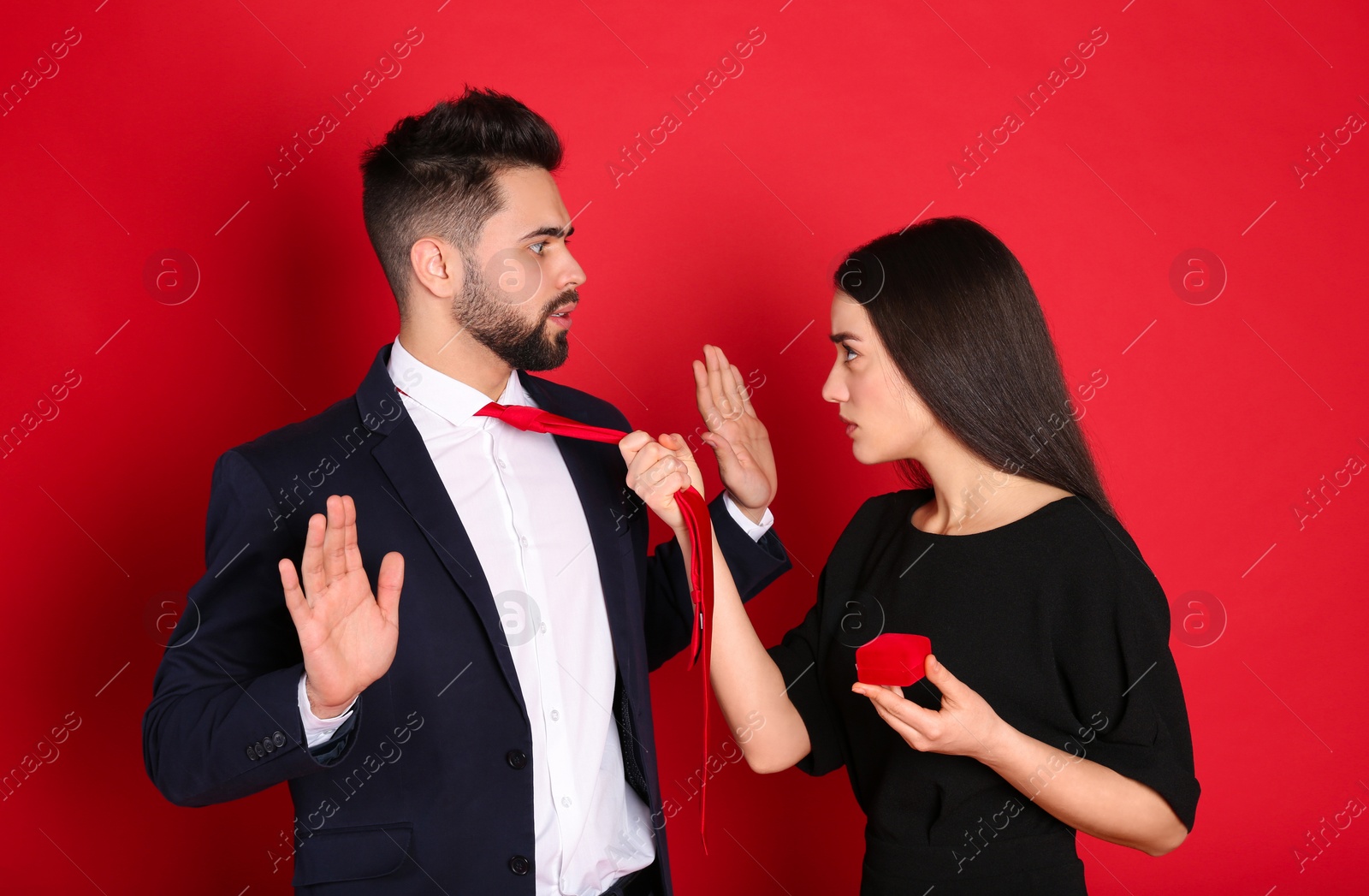 Photo of Young woman with engagement ring making marriage proposal to her boyfriend on red background