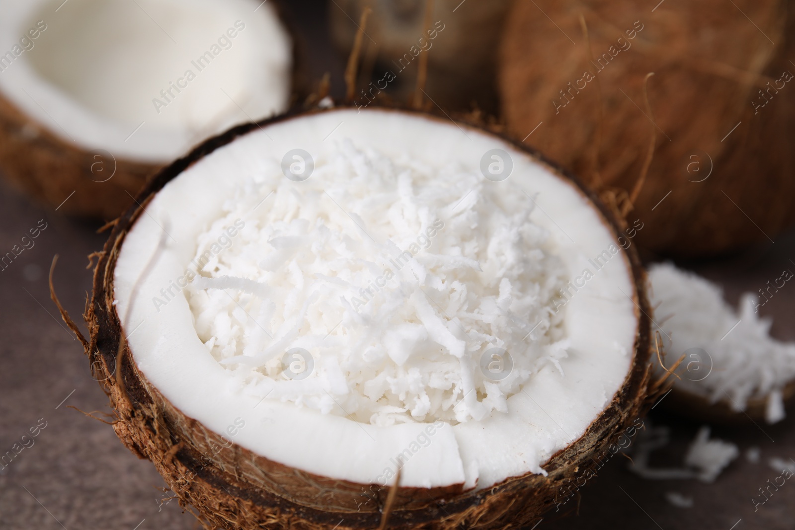 Photo of Coconut flakes in nut shell on brown table, closeup