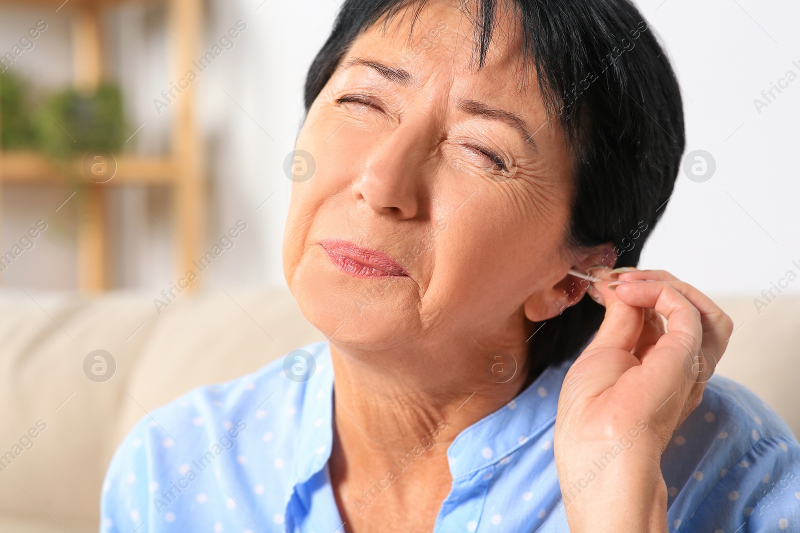 Photo of Senior woman cleaning ear with cotton swab at home, closeup