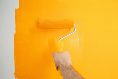 Photo of Man painting white wall with yellow dye, closeup. Interior renovation