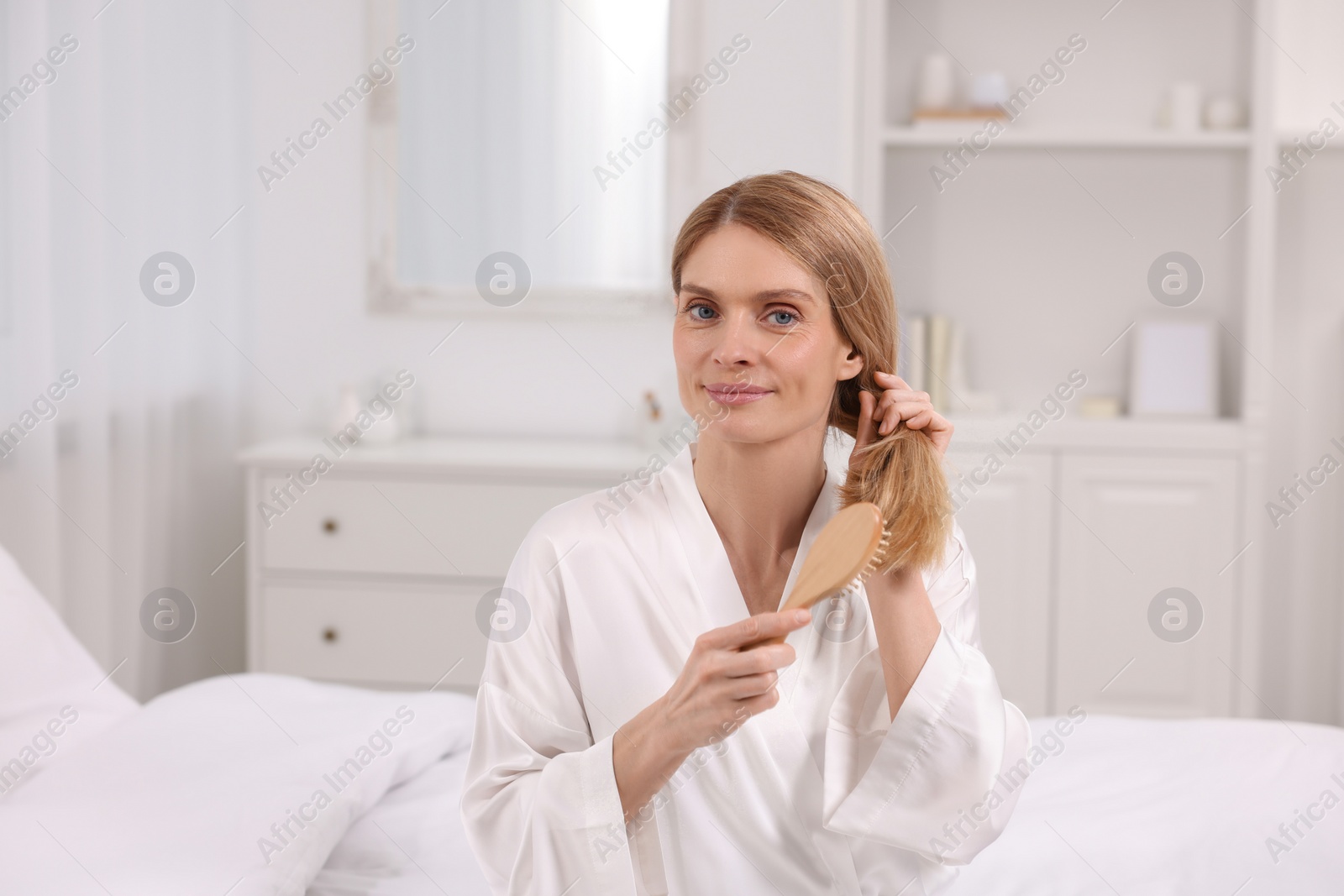 Photo of Beautiful woman brushing her hair on bed in room