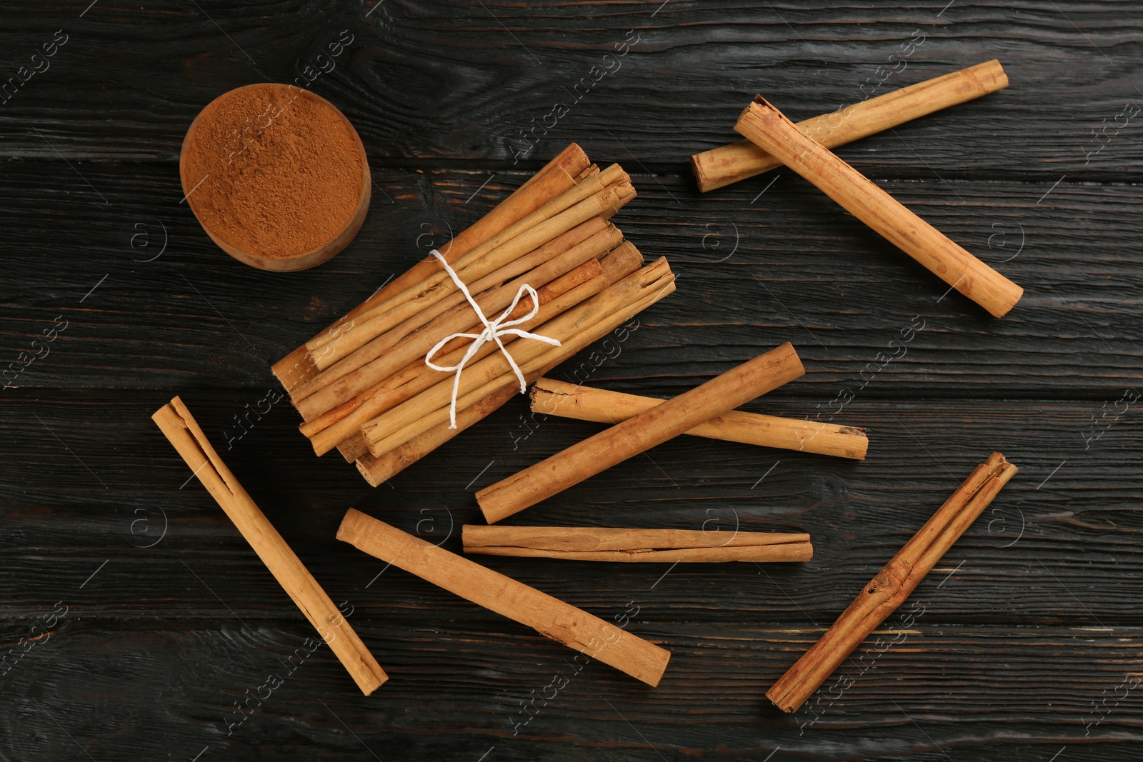 Photo of Aromatic cinnamon sticks and powder on black wooden table, flat lay