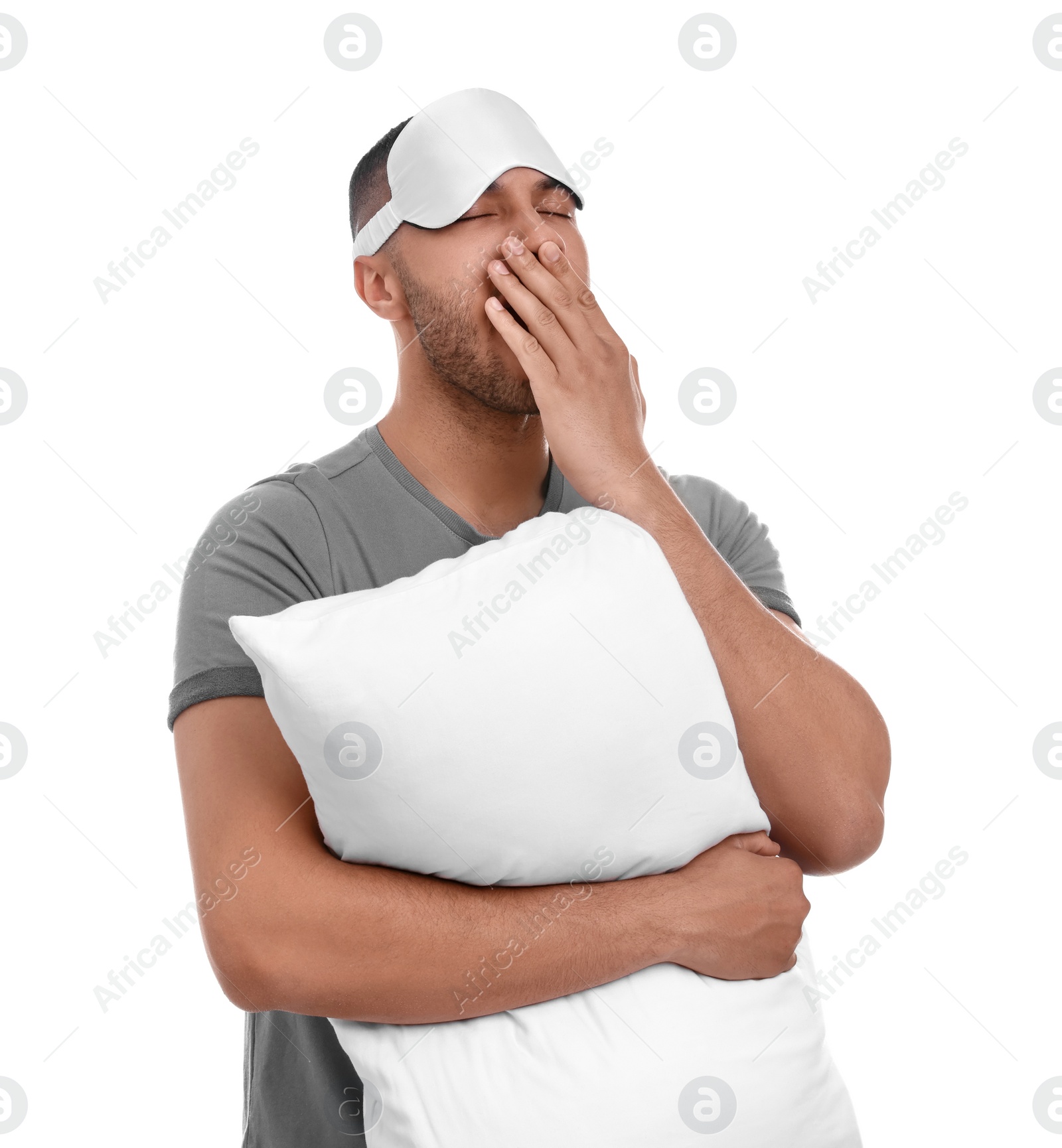 Photo of Tired man with pillow and sleep mask yawning on white background. Insomnia problem