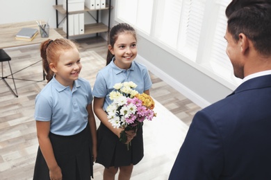 Photo of Schoolgirls with bouquet congratulating their pedagogue in classroom. Teacher's day