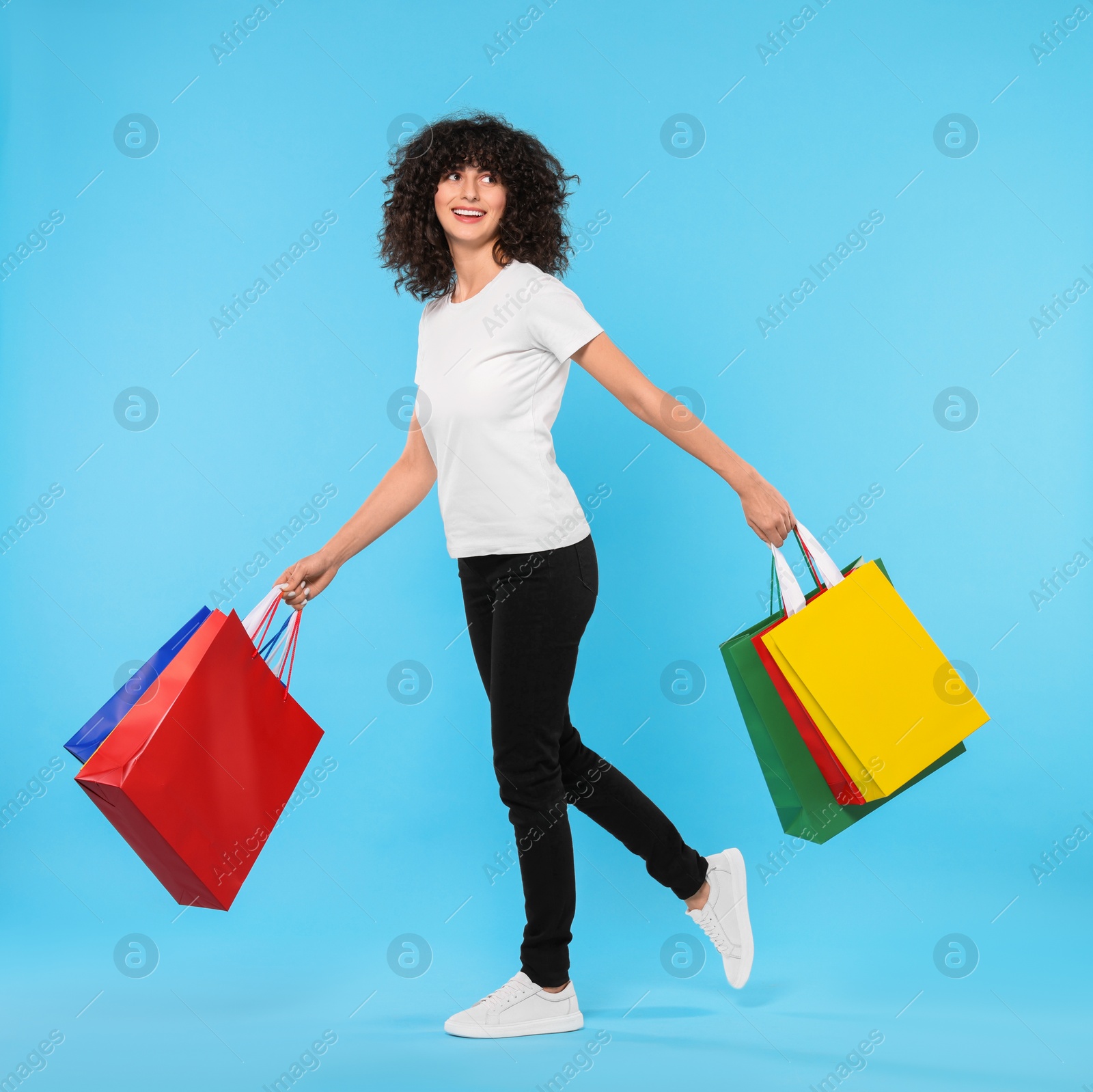 Photo of Happy young woman with shopping bags on light blue background