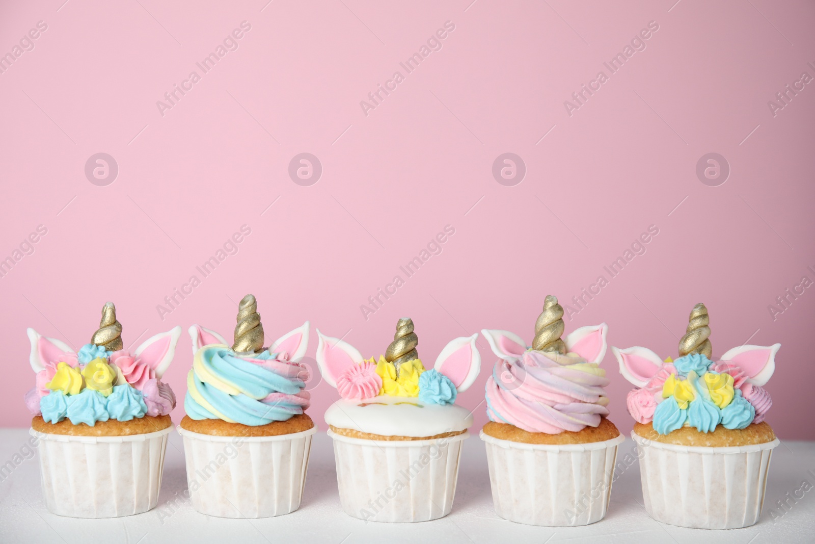 Photo of Many cute sweet unicorn cupcakes on white table against pink background