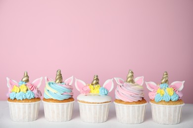 Photo of Many cute sweet unicorn cupcakes on white table against pink background