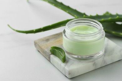 Jar with cream and cut aloe leaves on white table, closeup. Space for text