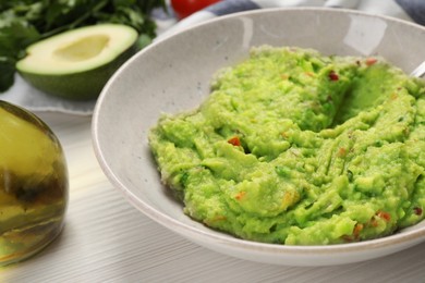 Delicious guacamole in bowl and ingredients on white wooden table, closeup