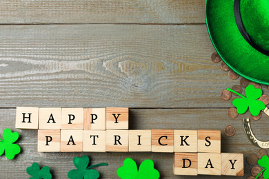 Photo of Wooden cubes with words HAPPY ST PATRICK'S DAY, horseshoe, gold coins and clover leaves on table, flat lay. Space for text