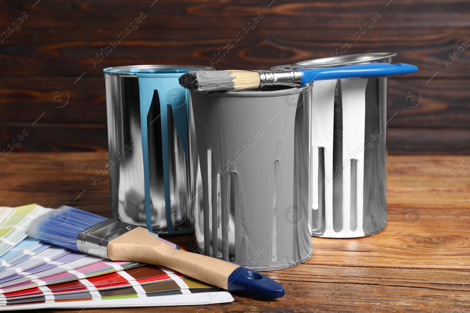 Photo of Cans of paints, brushes and color palette on wooden table