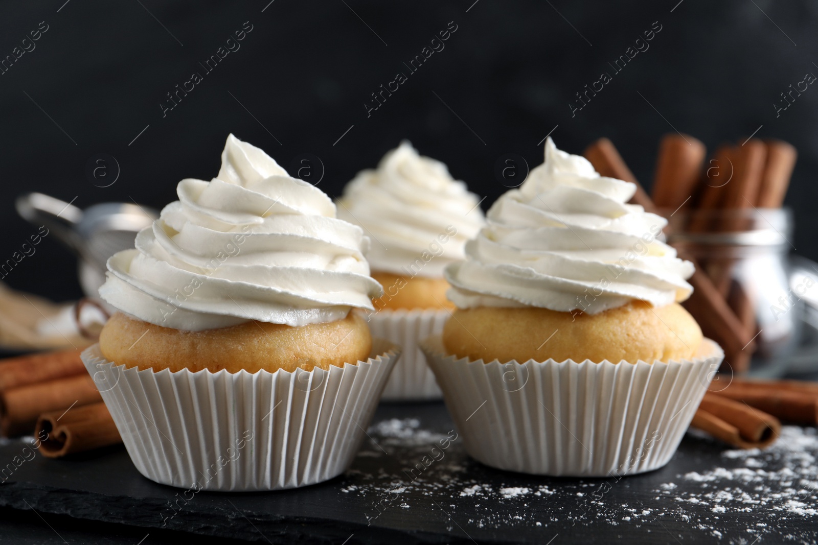 Photo of Delicious cupcakes with cream and cinnamon on slate board, closeup