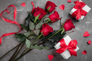 Photo of Flat lay composition with beautiful red roses and gift boxes on grey background. Valentine's Day celebration