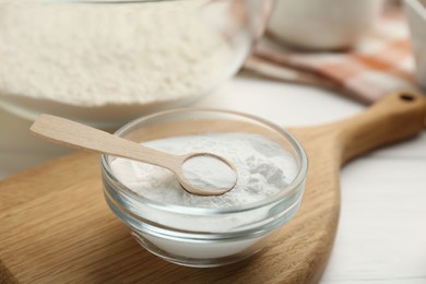 Baking powder in bowl and spoon on white table, closeup