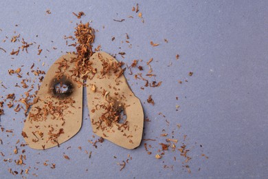 Photo of Paper cutout of human lungs with cigarette holes and tobacco on blue background, top view with space for text. No smoking concept