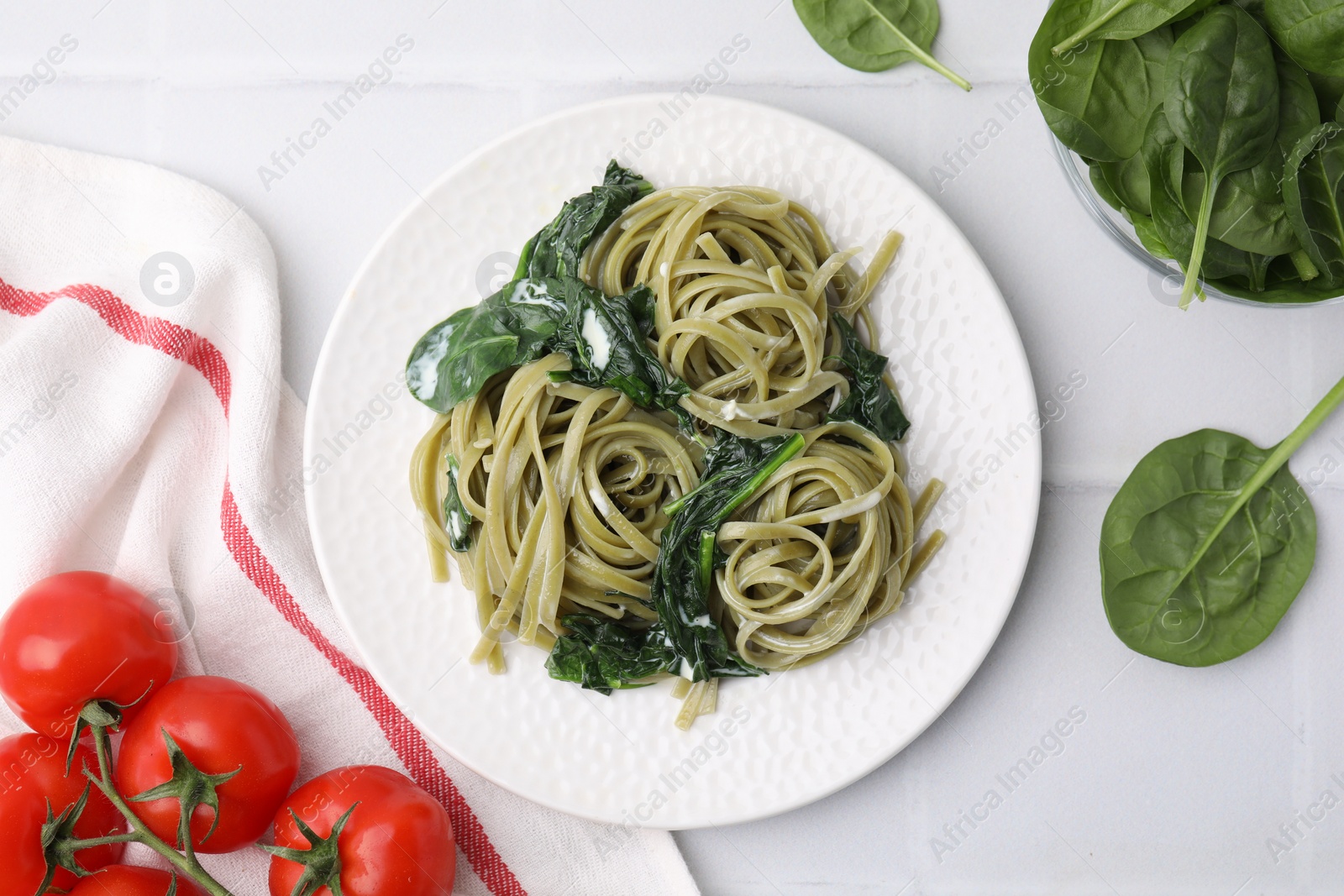 Photo of Tasty pasta with spinach, sauce and tomatoes on white tiled table, flat lay