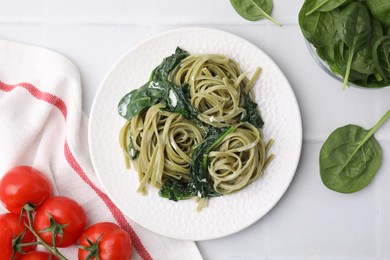 Photo of Tasty pasta with spinach, sauce and tomatoes on white tiled table, flat lay