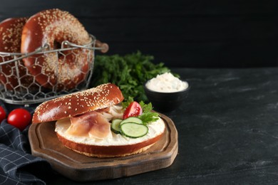 Photo of Delicious bagel with cream cheese, jamon, cucumber, tomato and parsley on black table