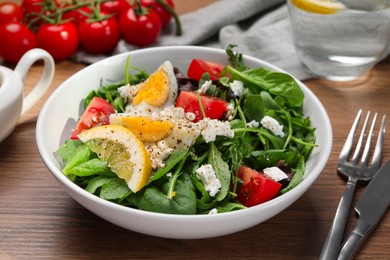 Photo of Delicious salad with boiled egg, tomatoes and cheese in bowl on wooden table, closeup