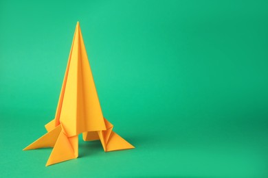 Origami art. Handmade yellow paper rocket on green background, space for text