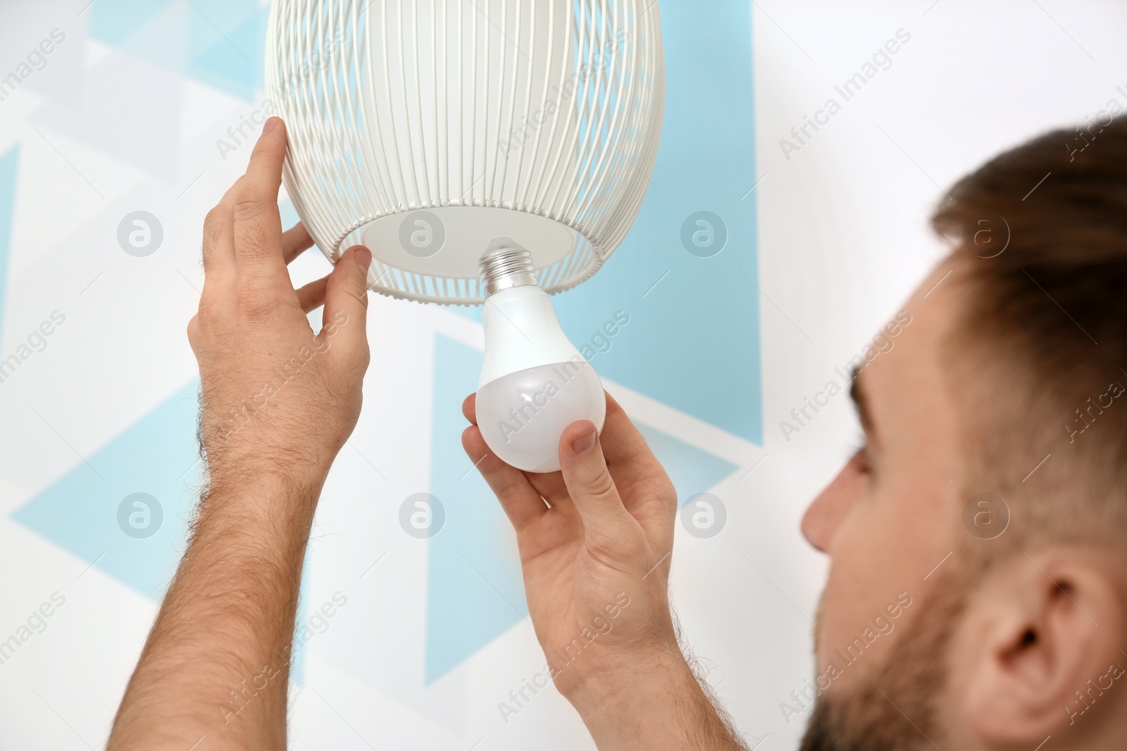 Photo of Man changing light bulb in lamp against color wall, closeup