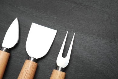 Photo of Cheese knives and fork on black background, flat lay. Space for text