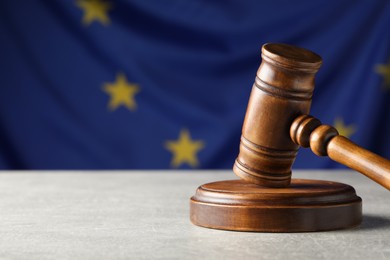 Photo of Wooden judge's gavel on grey table against European Union flag, closeup. Space for text