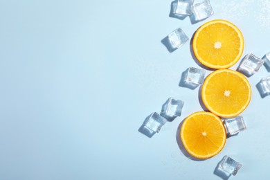 Photo of Slices of juicy orange and ice cubes on light blue background, flat lay. Space for text