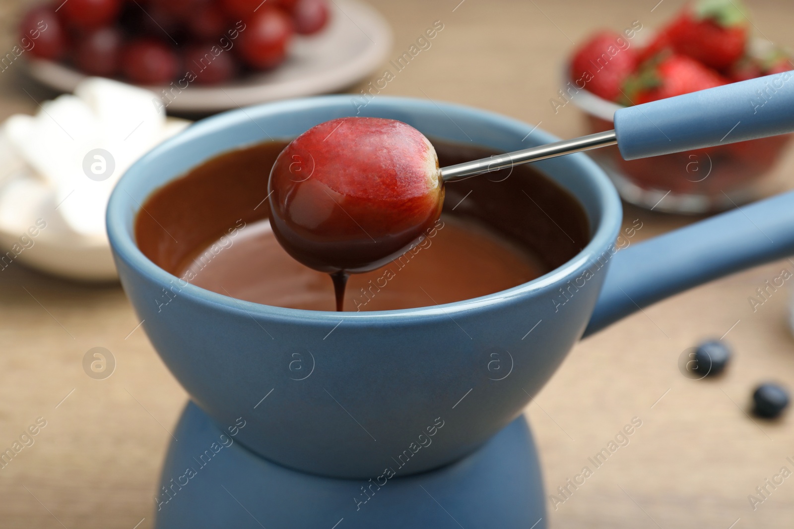 Photo of Dipping grape into pot with chocolate fondue on table, closeup