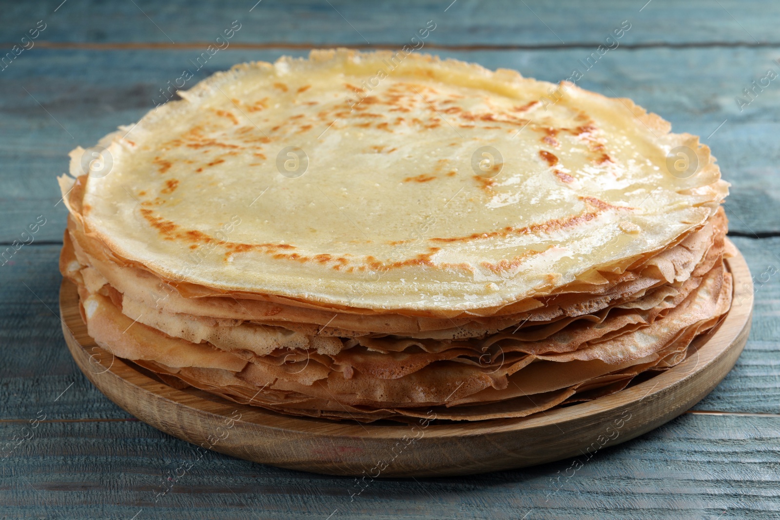 Photo of Stack of delicious crepes on blue wooden table, closeup