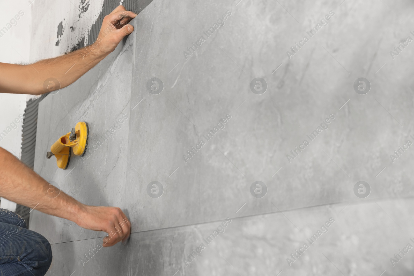 Photo of Worker installing wall tile with vacuum holder indoors, closeup