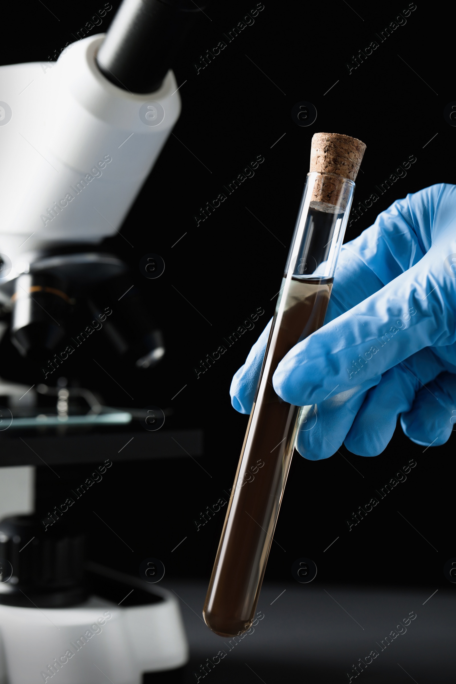 Photo of Scientist holding test tube with liquid against black background, closeup