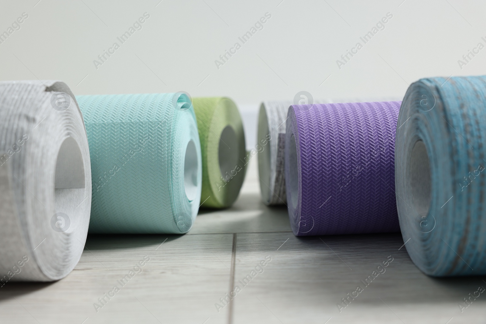 Photo of Many different wallpaper rolls on light wooden floor, closeup