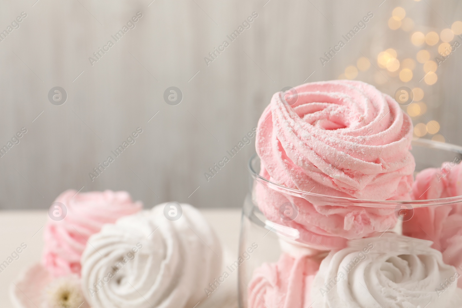 Photo of Delicious marshmallows in glass jar against blurred lights, space for text