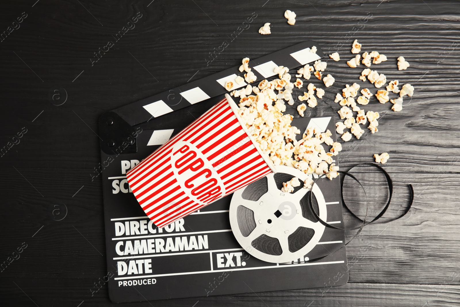 Photo of Tasty popcorn, film reel and clapperboard on wooden background, top view. Cinema snack