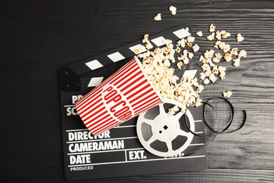 Photo of Tasty popcorn, film reel and clapperboard on wooden background, top view. Cinema snack