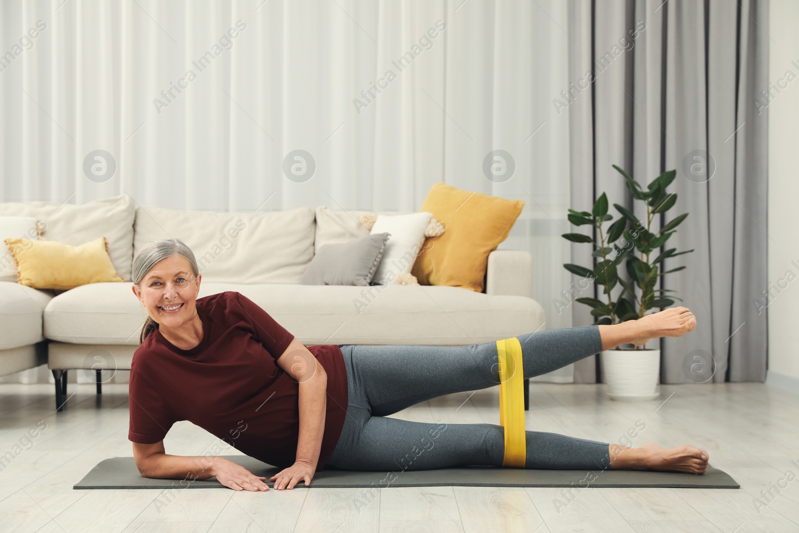 Photo of Senior woman doing exercise with fitness elastic band on mat at home