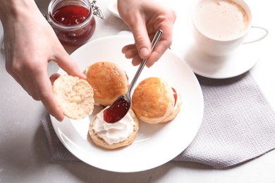 Photo of Woman spreading jam on tasty scones over table, closeup