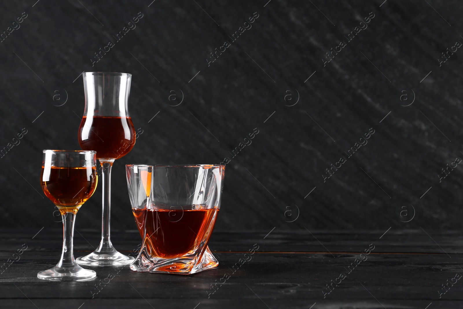 Photo of Different delicious liqueurs in glasses on black wooden table, space for text