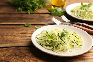 Photo of Tasty zucchini pasta with basil served on wooden table. Space for text