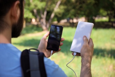 Photo of Man charging mobile phone with power bank in forest, closeup