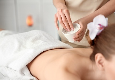 Photo of Beautiful young woman having massage with body scrub in spa salon
