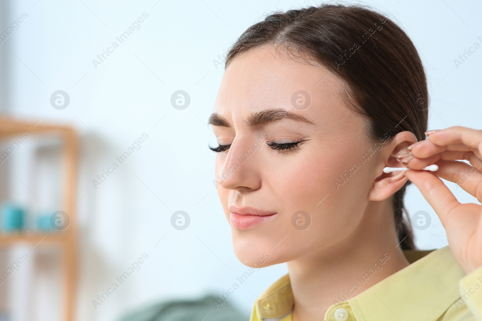 Photo of Young woman cleaning ear with cotton swab indoors